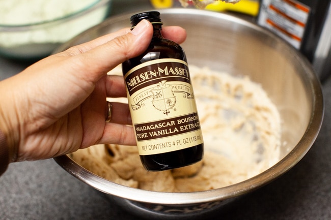 Hand holding bottle of vanilla extract with mixing bowl in background for Matcha Cookies from thelittlekiitchen.com