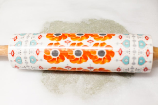 Matcha Cookie dough being rolled out under parchment paper with colorful rolling pin from thelittlekiitchen.com