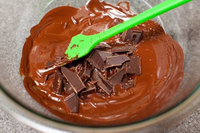 Stirring melted chocolate in a glass bowl with a green spatula from thelittlekiitchen.com