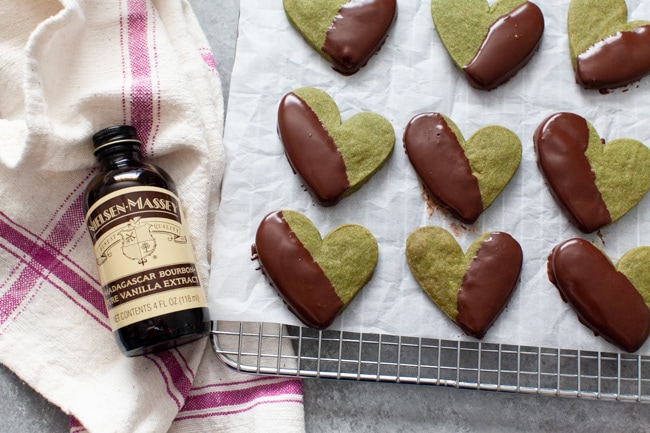 Heart Shaped Chocolate Dipped Matcha Cookies on cooling rack next to bottle of vanilla extract from thelittlekiitchen.com