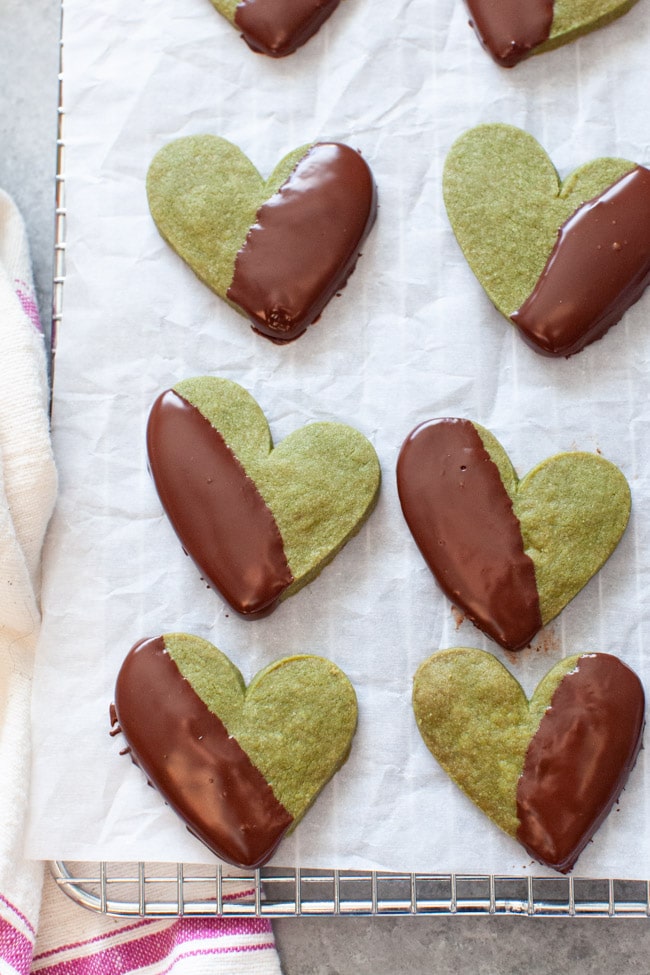 Heart Shaped Matcha Cookies Dipped in Chocolate on White Parchment Paper from thelittlekiitchen.com