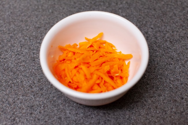 Small white bowl full of shredded carrots on gray countertop for Vegetarian Dumplings from thelittlekiitchen.com