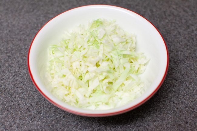 White and red bowl filled with sliced cabbage on gray countertop from thelittlekiitchen.com