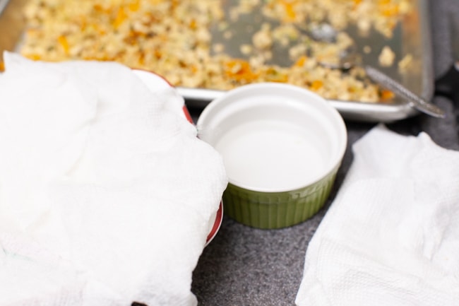 Damp towels over dumpling wrappers to keep them moist with small bowl of water and dumpling filling in background from thelittlekiitchen.com