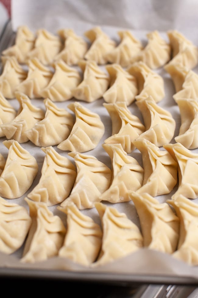 Parchment-lined baking sheet with uncooked Vegetarian Dumplings from thelittlekiitchen.com