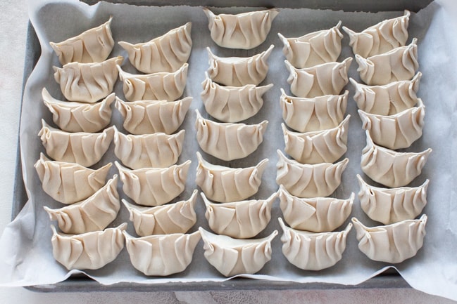 Parchment-lined baking sheet with uncooked Vegetarian Dumplings lined up from thelittlekiitchen.com