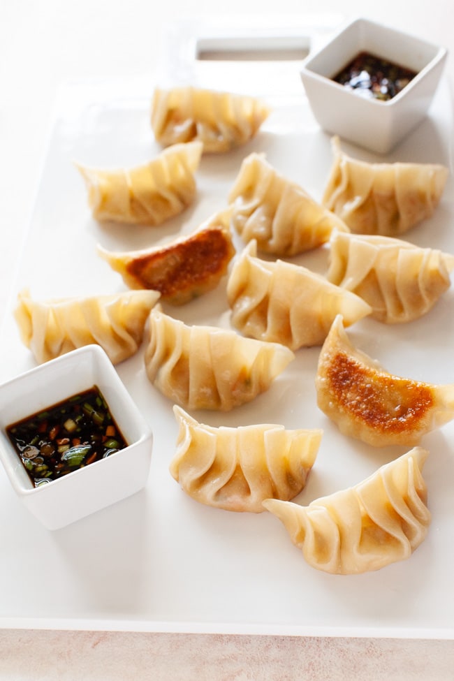 Vegetarian Dumplings on white serving board with two square cups filled with dipping sauce from thelittlekiitchen.com
