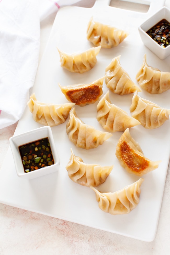 Vegetarian Dumplings from thelittlekiitchen.com Vegetarian Dumplings on a white serving board with two square cups filled with dipping sauce from thelittlekiitchen.com