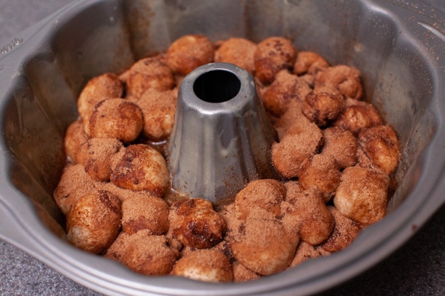 Monkey Bread dough in a bundt pan topped with butter and a cinnamon sugar mixture.