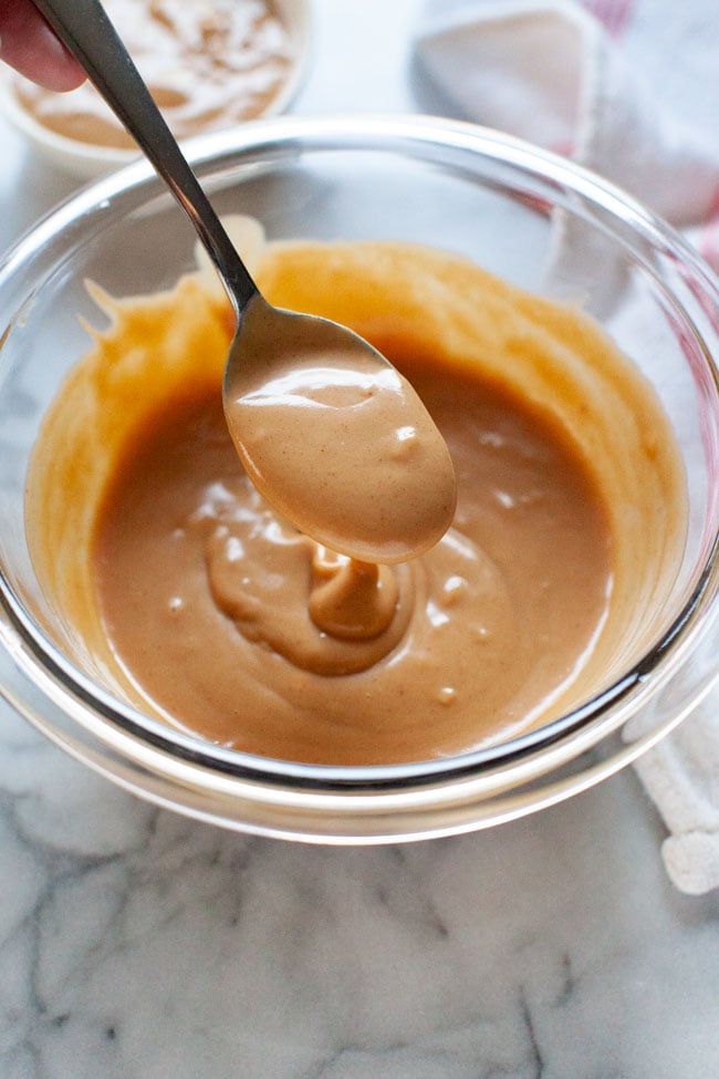 Peanut Sauce from thelittlekiitchen.com peanut sauce on a spoon over a glass bowl with a napkin in the background