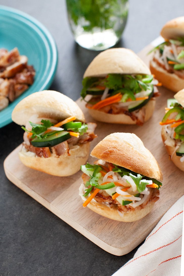 Lemongrass Chicken Banh Mi Sliders from thelittlekiitchen.com chicken banh mi sliders on a wooden board with a plate of chicken in the background